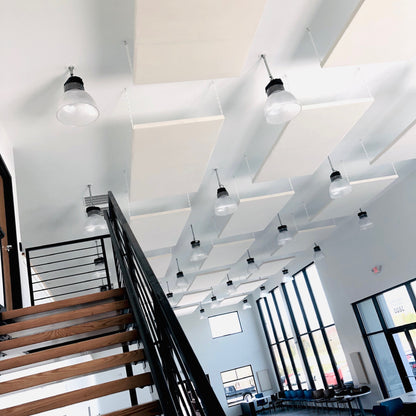 White acoustic ceiling panels installed in a modern loft-style office space with a wooden staircase, black metal railings, and multiple pendant light fixtures.